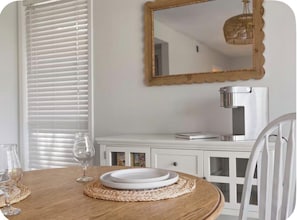 Un comedor con una mesa redonda, sillas blancas, un armario blanco y un espejo en la pared.