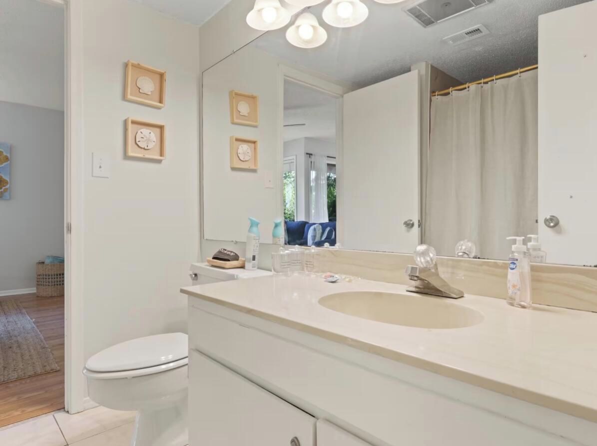 A bathroom with a white sink, mirror, and toilet. There are framed pictures on the wall and a shower curtain.