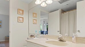 Ein Badezimmer mit weißem Waschbecken, Spiegel und Toilette. An der Wand befinden sich Bilder in Rahmen und ein Duschvorhang.