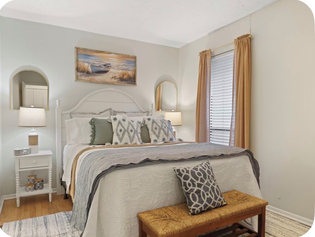A bedroom with a bed, bedside tables, a bench, a painting, and a window with curtains.