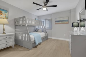 A bedroom with a bunk bed, a ceiling fan, a bedside table with a lamp, and a dresser. - Beachfront Islands End Condo | Gorgeous Big Carlos Pass Views | Heated Pool + Hot Tub | Free Parking (Fort Myers Beach)