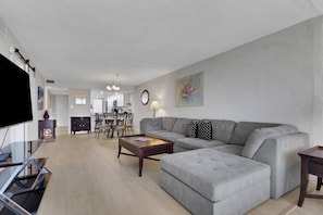 A modern living room with a grey sofa, a coffee table, and a TV. - Beachfront Islands End Condo | Gorgeous Big Carlos Pass Views | Heated Pool + Hot Tub | Free Parking (Fort Myers Beach)