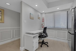A modern office space with a white desk, black office chair, and a white cabinet. There is a fire extinguisher mounted on the wall and a window with blinds. - Beachfront Islands End Condo | Gorgeous Big Carlos Pass Views | Heated Pool + Hot Tub | Free Parking (Fort Myers Beach)