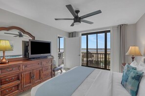 Ein Hotelzimmer mit Bett, Fernseher, Schminktisch, Deckenventilator und einem Balkon mit Blick auf das Wasser.
