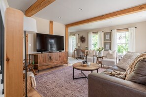Ein geräumiges Wohnzimmer mit einem großen Flachbildfernseher, einer Holzunterhaltungsecke, einem runden Couchtisch und einem gemütlichen Sofa.
