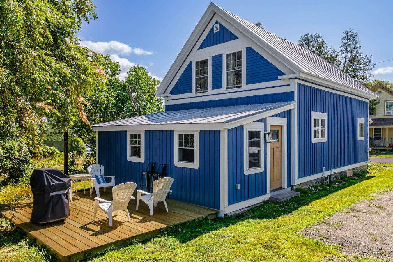 A blue house with a deck, outdoor seating, and a barbecue grill.