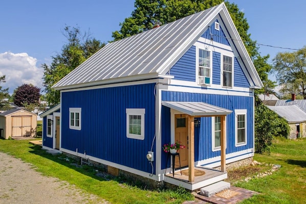Ein eingeschossiges blaues Haus mit Satteldach, einer Veranda und einer kleinen angeschlossenen Garage.