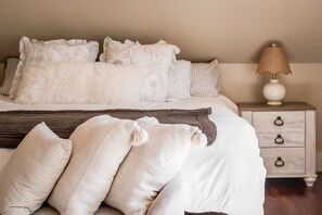 Un letto rifatto con lenzuola bianche e cuscini decorativi, una coperta marrone e un comodino con una lampada.