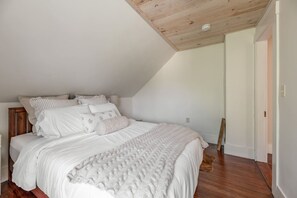 Ein Schlafzimmer mit schrägem Dach, einem Bett mit weißer Bettwäsche und einem Holzboden.