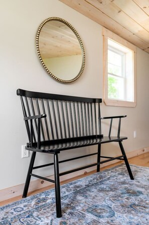 A black metal bench with a beaded frame against a wall, a window with natural light, and a patterned rug on the floor. - The Blue House Hideaway | Less than 20 Minutes to Sugarloaf (Kingfield)
