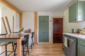 Eine Küche mit Holzboden, einem Esstisch mit Stühlen, einer grünen Tür und einer kleinen Kücheninsel mit einem Toaster.