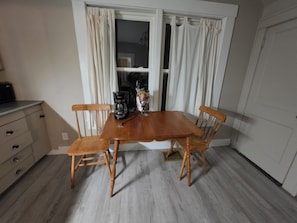 Een eetruimte met een houten tafel en stoelen, een koffiezetapparaat en een raam met gordijnen.