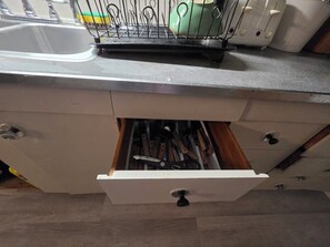 Een keuken met een spoelbak, een afdruiprek en een lade met bestek.