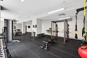 Ein moderner Fitnessraum mit verschiedenen Trainingsgeräten, darunter ein Squat-Rack, eine Hantelbank und Widerstandsbänder.