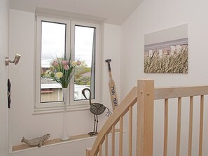 A room with a white door, a window with a view of the outside, a wooden staircase, and a painting on the wall. - Holiday Home in Duhnen With Wi-fi and Parking (Cuxhaven)