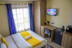 Hotellihuone, jossa on sänky, työpöytä, tuoli, televisio ja kahvinkeitin.