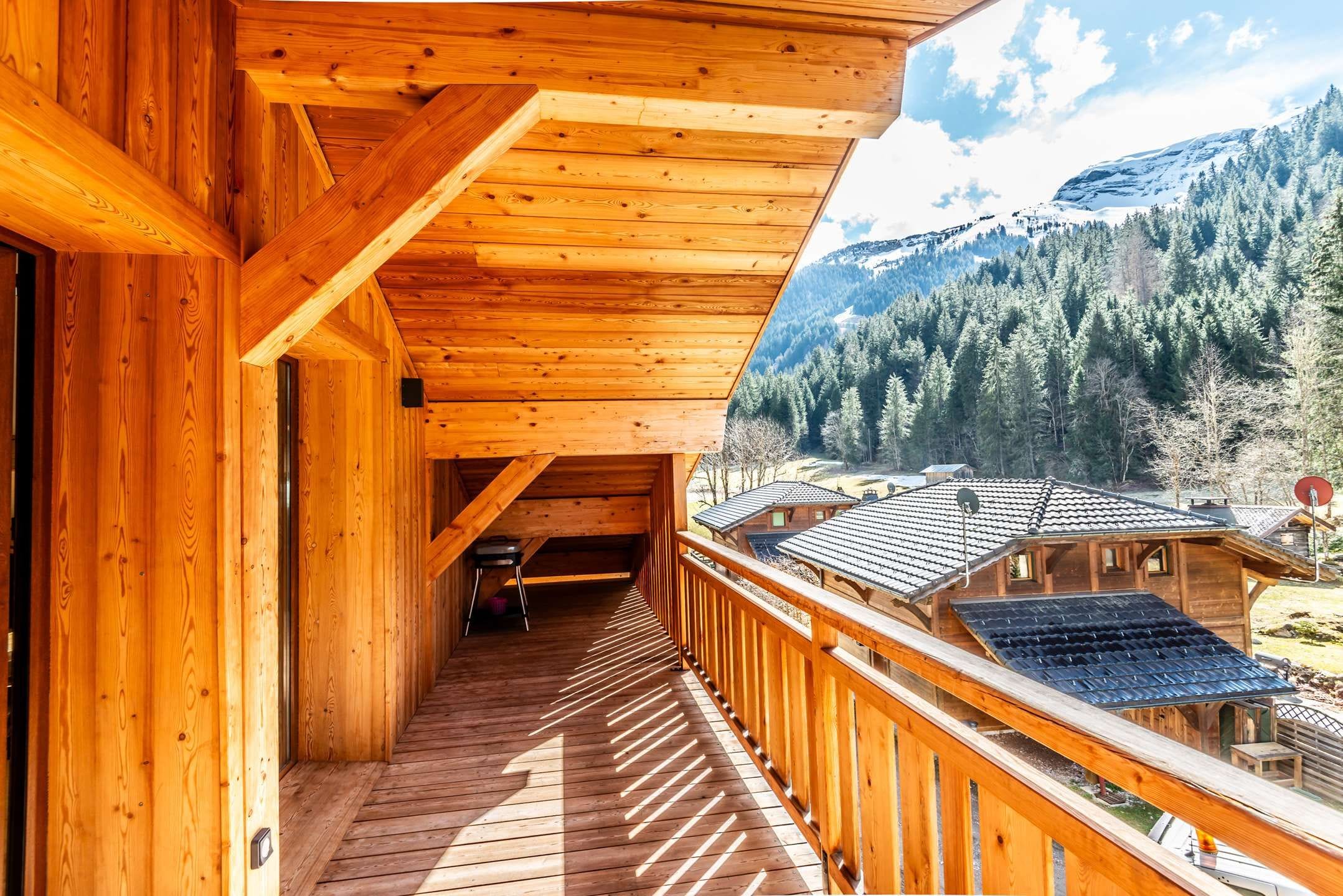 A wooden balcony with a view of a mountainous landscape and traditional buildings.