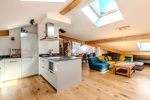 Een modern loft-appartement met een open keuken en woonruimte, voorzien van een dakraam en houten balken.