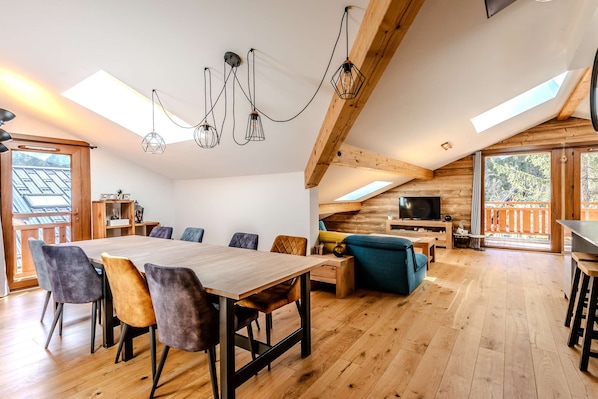 Een ruime woonkamer met een houten eettafel, meerdere stoelen, een bank en een televisie.