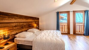Une chambre à coucher avec une tête de lit en bois, un lit recouvert de linge de lit blanc, une lampe de chevet et une vue sur un balcon avec des rideaux bleus.
