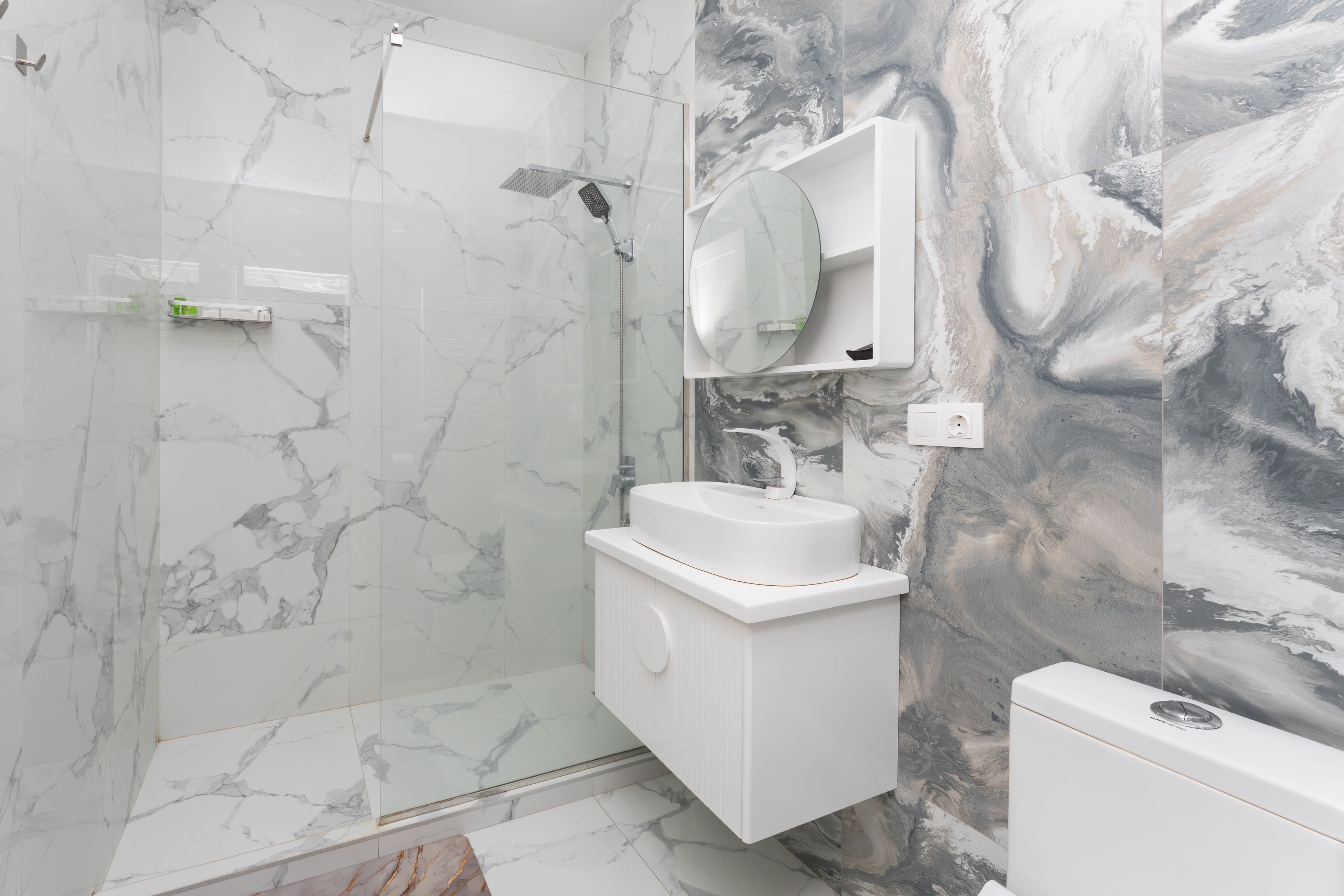 A modern bathroom with a glass shower enclosure, a white sink, and a marble-patterned wall.
