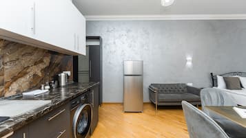 A modern kitchen with a marble countertop, a washing machine, a refrigerator, and a grey sofa in a compact living space.