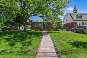 A residential property with a brick house, a paved driveway, and a lawn. - Peaceful, cozy, with room for 8,  Lilly's Pad is an ideal Brantford stay. (Brantford)