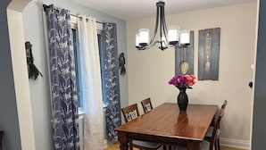 A dining room with a wooden table, chairs, a vase with flowers, a chandelier, and curtains.