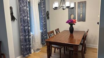 A dining room with a wooden table, chairs, a vase with flowers, a chandelier, and curtains.