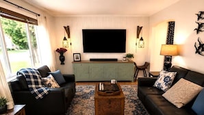 A living room with a large flat-screen TV, two sofas, a coffee table, and a patterned rug.