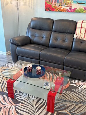 Ein schwarzes Ledersofa mit einem Glastisch davor, ein gemustertes Teppich und ein Strandbild an der Wand.
