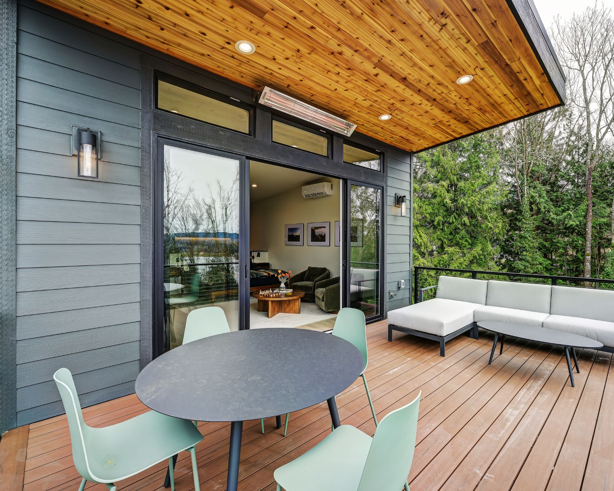 A modern outdoor deck with a round table and chairs, a sofa, and a wooden ceiling.