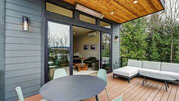 A modern outdoor deck with a round table and chairs, a sofa, and a wooden ceiling.