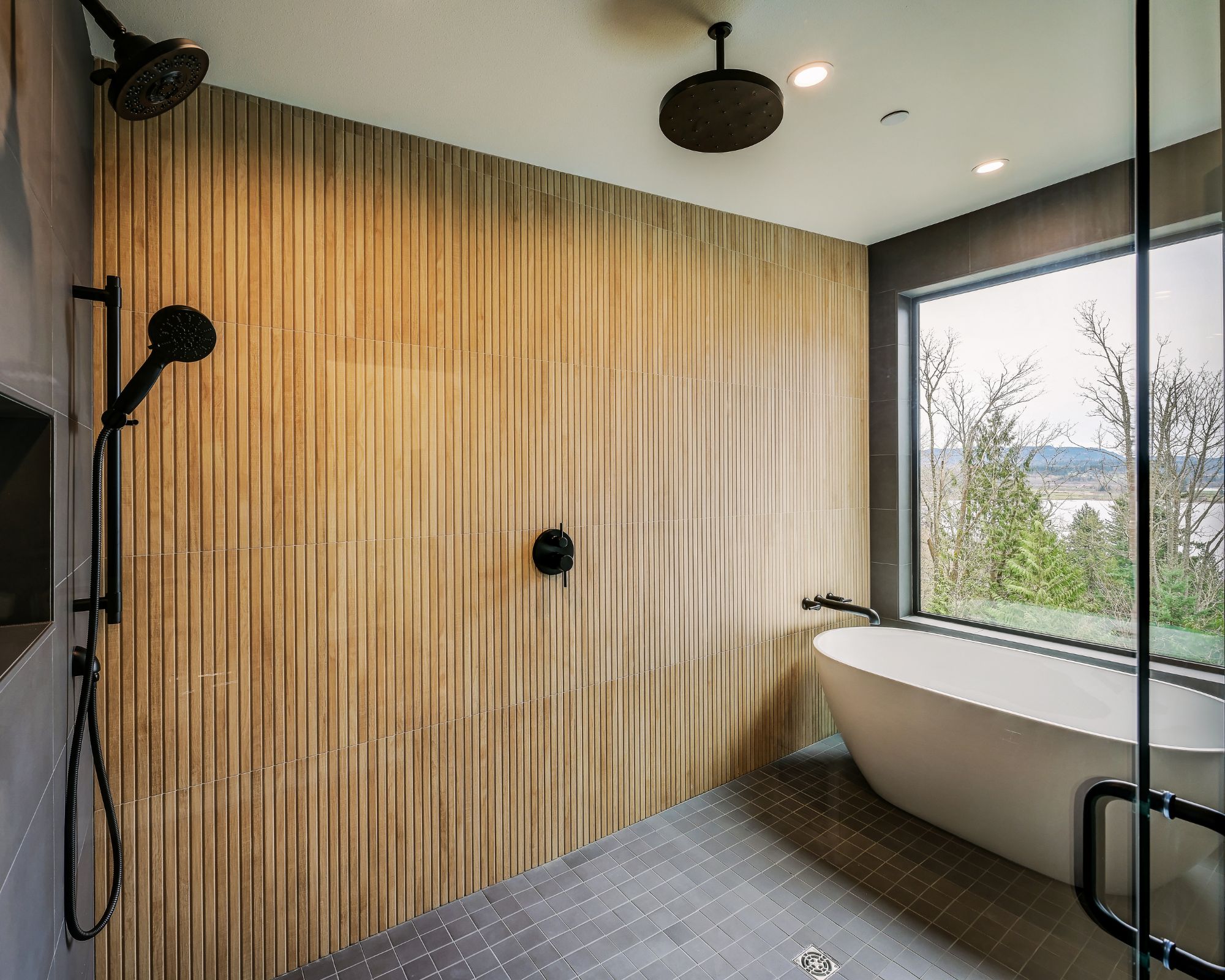 Een moderne badkamer met een wand van houten latten, een vrijstaand bad en een douchegedeelte met een handdouche.