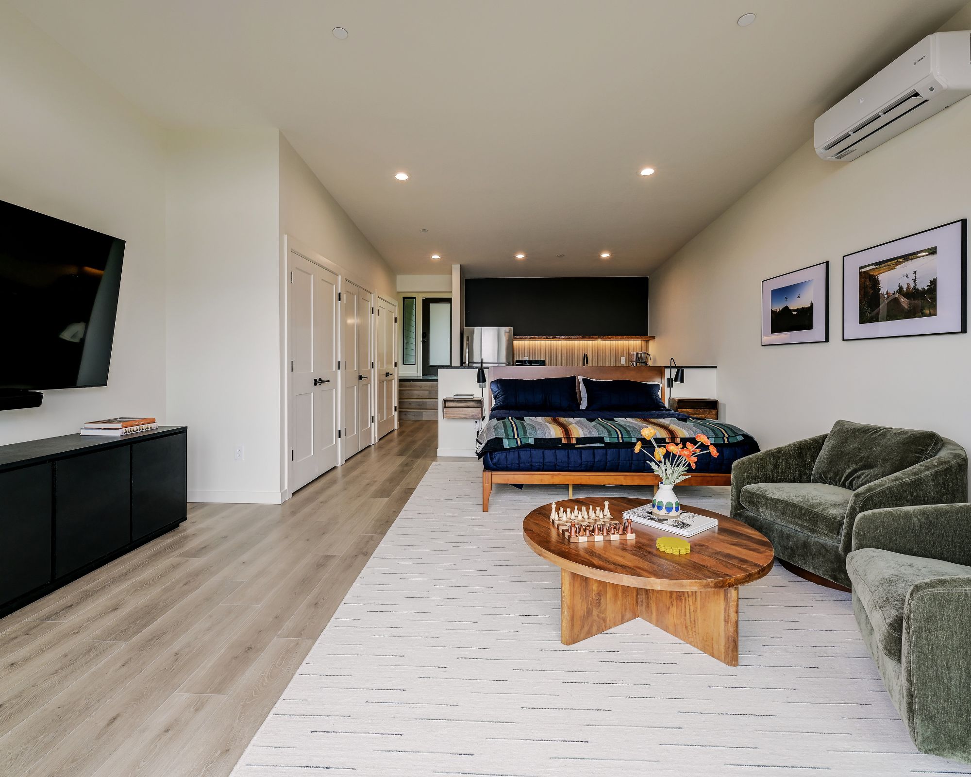 A modern living room with a flat-screen TV, a sofa, a coffee table, and a dining area in the background.