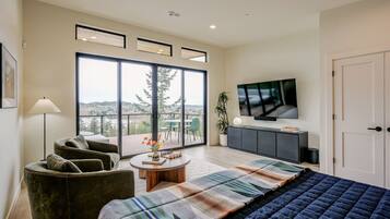 A modern bedroom with a large bed, a sofa, a TV, and a view of the outdoors.