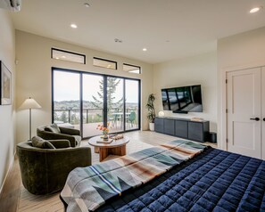 A modern bedroom with a large bed, a sofa, a TV, and a view of the outdoors.