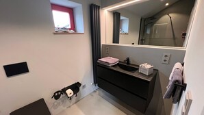 A modern bathroom with a large mirror, a black vanity, a window, and a shower. - Vulkaneifel Artists' House (Mückeln)