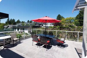 Un patio al aire libre con una mesa y sillas, un paraguas rojo y vistas a casas al fondo.