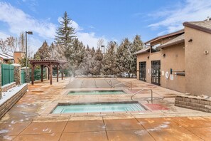 A spa area with two hot tubs, a covered seating area, and a building with a door and windows. - Park City Getaway | Pool Access + Near Skiing (Park City)