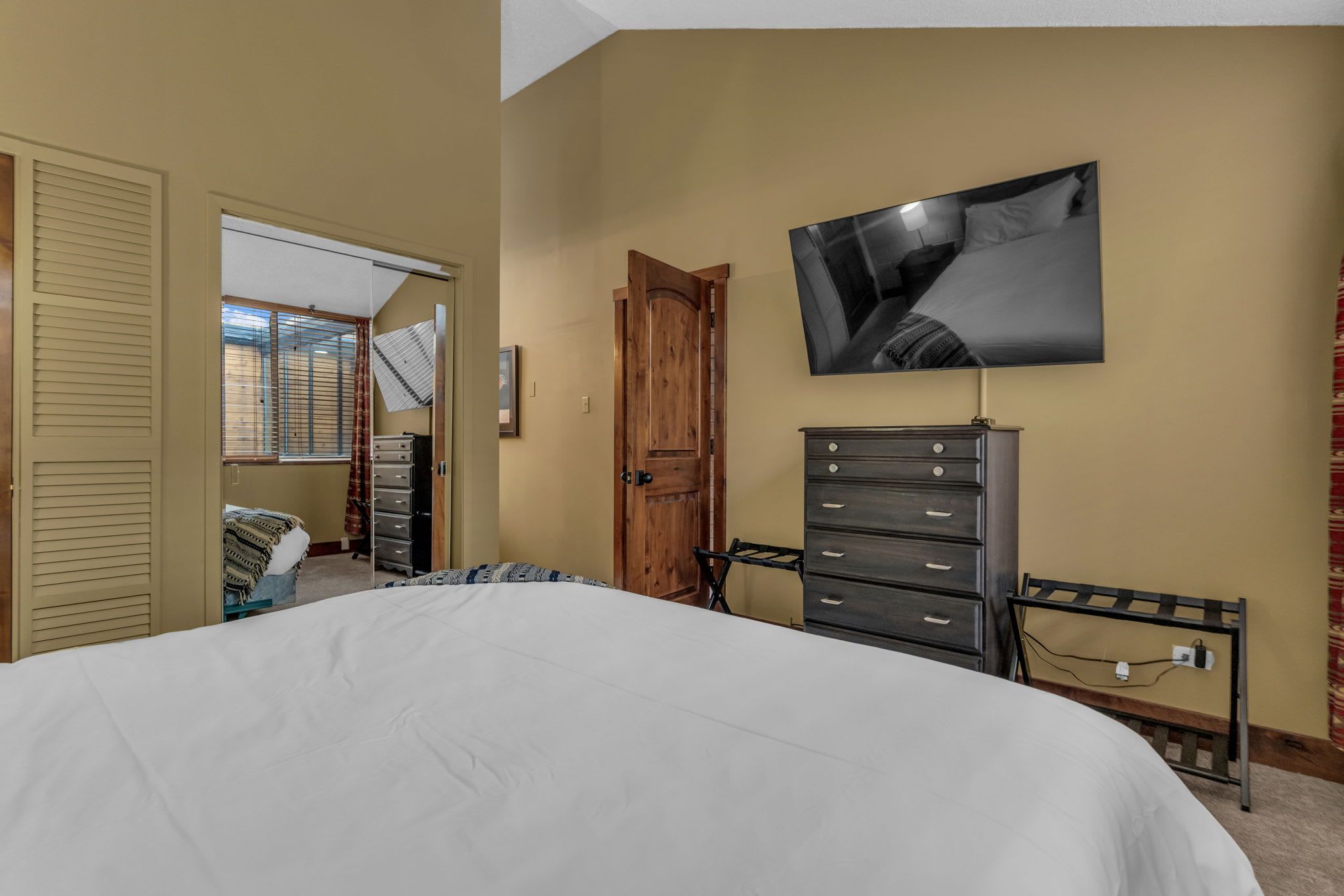 Un dormitorio con una cama grande, una puerta de madera, un aparador y un televisor montado en la pared.