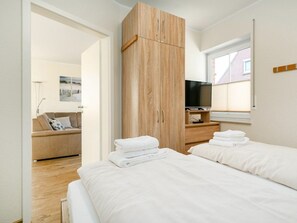 Ein modernes Schlafzimmer mit einem Holzschrank, einem Flachbildfernseher und einem Bett mit ordentlich gefalteten weißen Handtüchern.