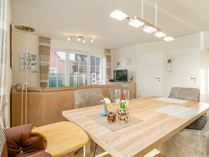 Ein modernes Wohnzimmer mit einer Couch, einem Esstisch mit Stühlen, einem Fernseher und einem großen Fenster.