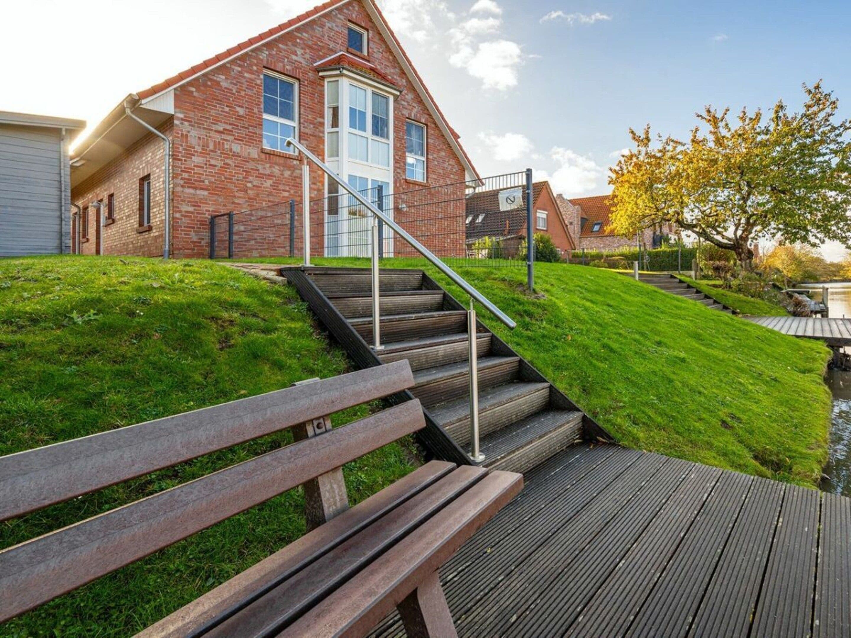 A residential building with a brick facade, a set of wooden stairs leading to a deck, and a grassy area.