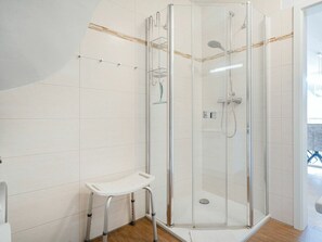 Ein modernes Badezimmer mit einer gläsernen Duschkabine, einem weißen Fliesenboden und einem kleinen weißen Hocker.