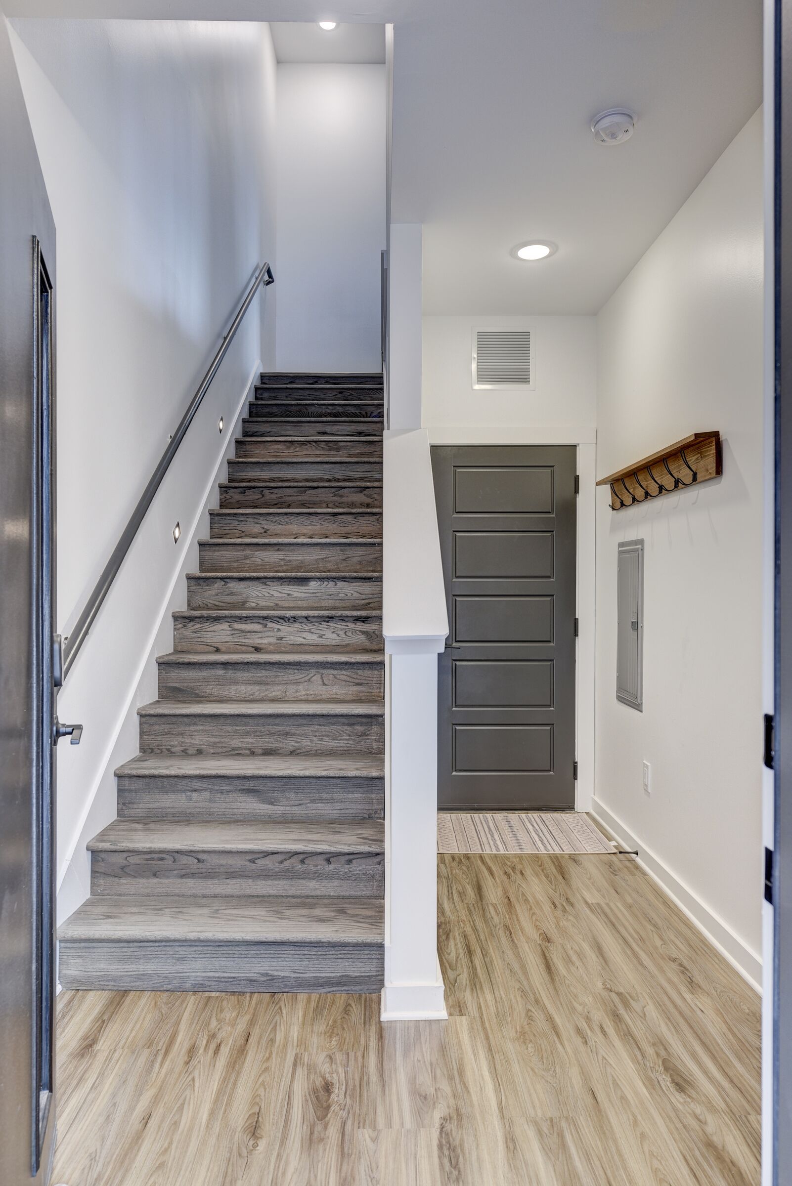 A staircase with wooden steps and a metal handrail leading to a landing with a door and a wall-mounted light fixture.
