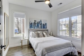 Un dormitorio con cama, ventilador de techo, un cuadro y ventanas amplias.
