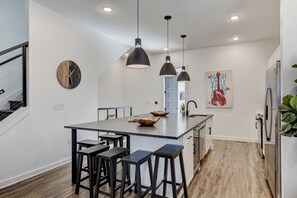 Una cocina moderna con una isla central, iluminación colgante y un reloj de pared.