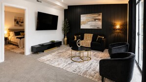 A modern living room with a black sofa, a round coffee table, and a flat-screen TV mounted on the wall. - Modern 4-bedroom house  with Country Vibes. (Belton)