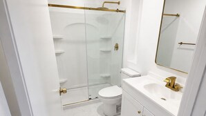 A bathroom with a glass-enclosed shower, a white toilet, and a vanity with a gold faucet. - Modern 4-bedroom house  with Country Vibes. (Belton)